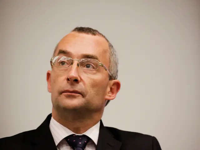 In this picture there is a man wearing a suit. In the background it is well.