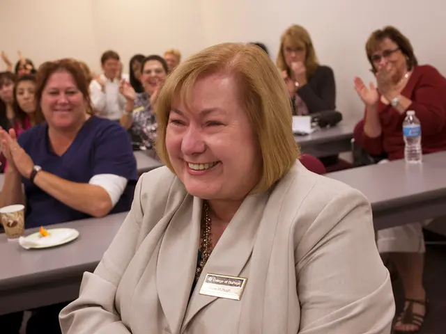 In this picture there is a women sitting on the chair wearing a cream color suit, smiling and...