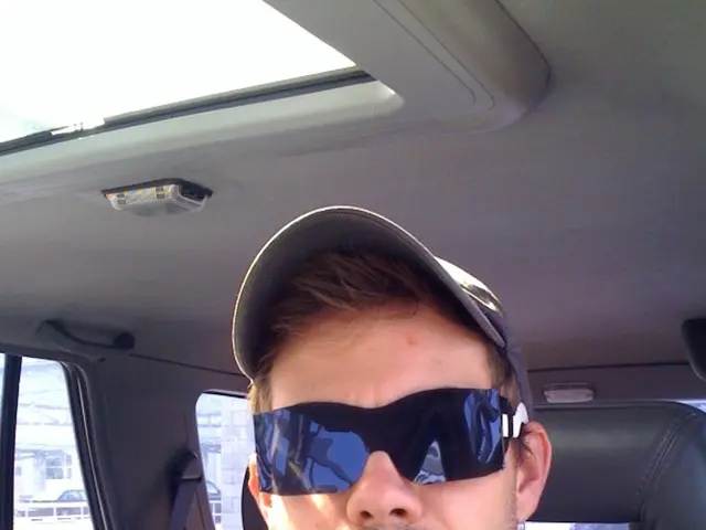 In this picture we can see a man, he wore spectacles and a cap, and he is seated in the car.