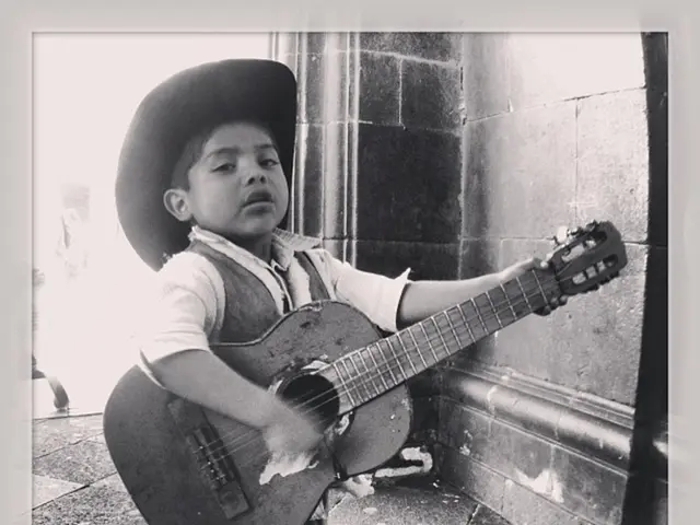 This is a black and white pic. Here we can see a boy is standing on the floor and holding a guitar...
