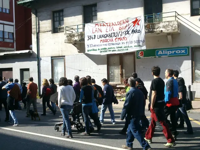 In this image, we can see buildings. There are persons walking on the road. There is a banner at...