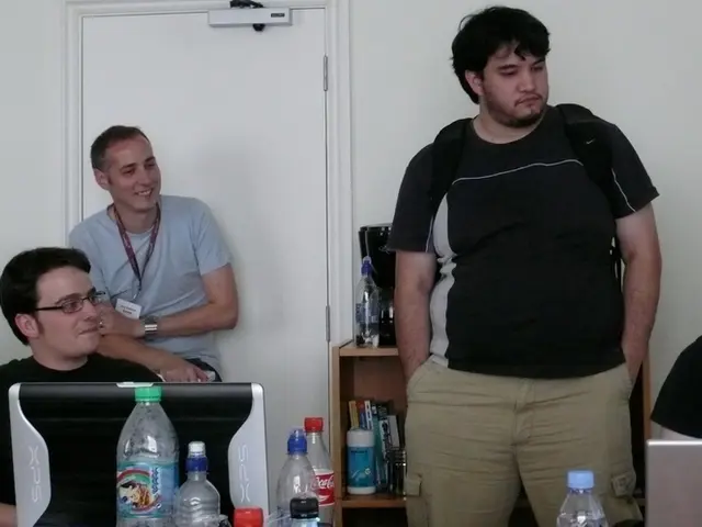 In this image I see 5 men, in which 3 of them are sitting and rest of them are standing. I can also...