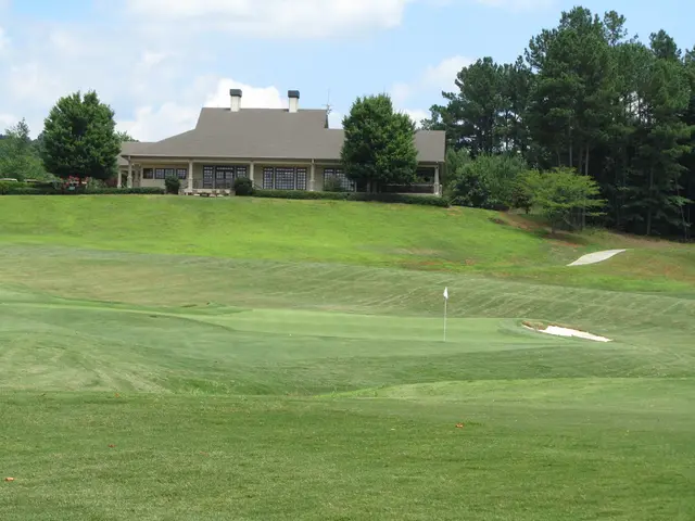 In this image there is a golf court , in the background there is a house, trees and a sky.