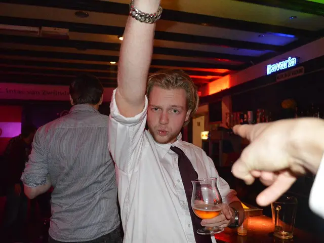 In this Picture we can see that group of person standing in the bar, and in front a man wearing...