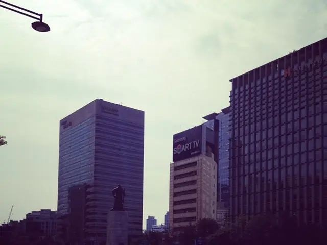 In this image there are cars passing on the road, beside the cars there is a fountain, beside the...