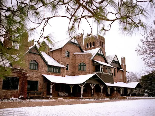 There is a building with windows, pillars and chairs. On the right there is a bench and a branch....
