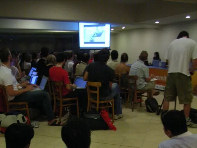 This image is clicked inside the hall. In this image there are few people sitting in the chairs and...