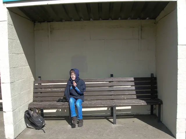 In the image there is a bus stop and there is a bench on which a boy sat with a hoodie and there is...