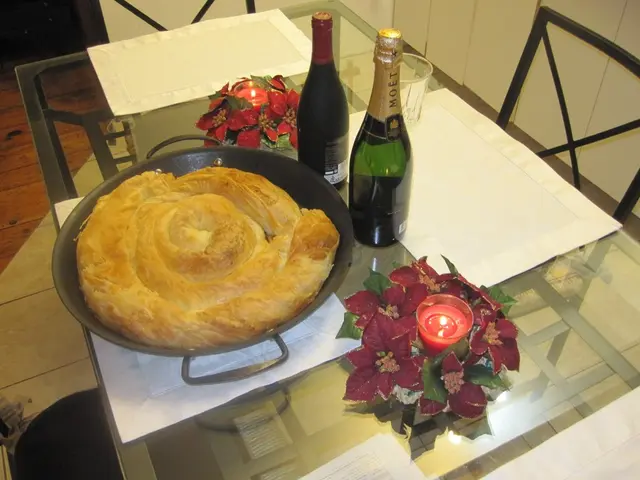 On the table there are wine bottles,candles,glass,flower vase and food in a bowl. In the background...