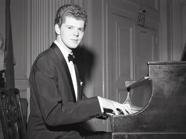 in this image there is a man sitting in the chair and playing a piano and in the back ground there...