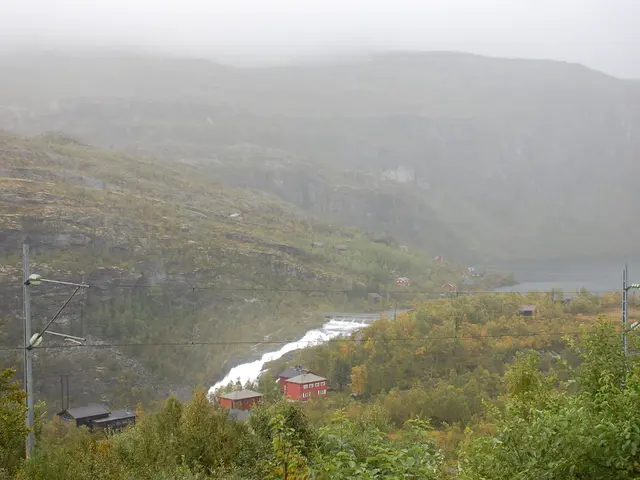 In the image we can see electric pole and electric wires. There are even buildings and the river....