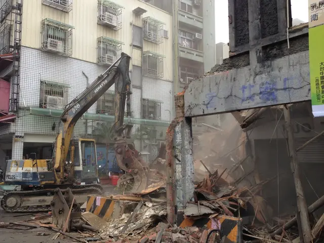 In this picture we can see an excavator on the road, banners, buildings with windows and in the...