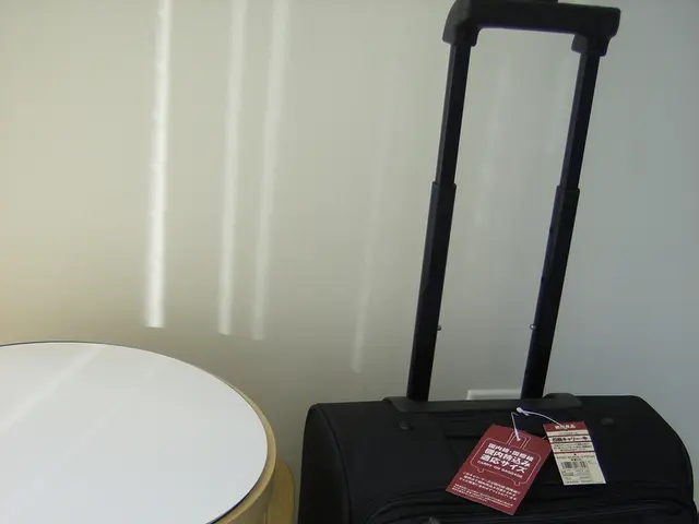 There is a black suitcase and labels are on top of it. There is a brown color stool beside it.