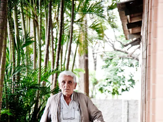 In this image i can see an old man walking. He is holding a newspaper. He is wearing a pair of...