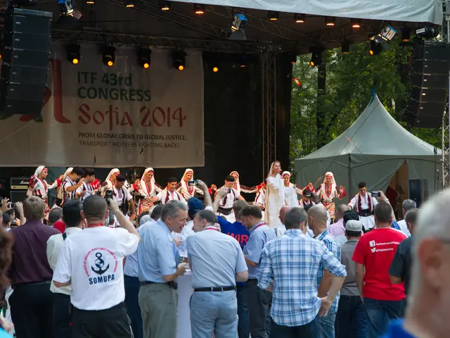 Here we can see people. Background there is a tent, focusing lights, speakers, hoarding and trees.