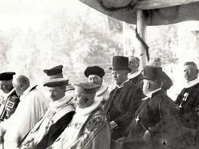 This is a black and white picture. Here, we see many people sitting on chairs under the tent. There...