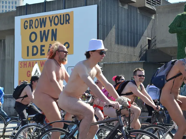 This is the picture taken in the outdoors. A group of people riding their bicycles on road. Behind...