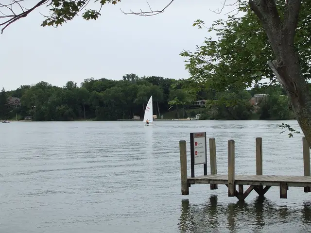 There are two boats on water and there are trees and buildings in the background.