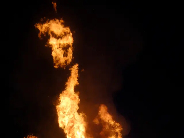 In this picture I can see fire and few people standing, looks like a house caught fire and I can...