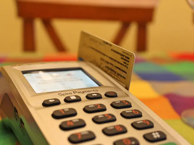 The image shows a credit card machine sitting on top of a colorful table, with a card placed on...