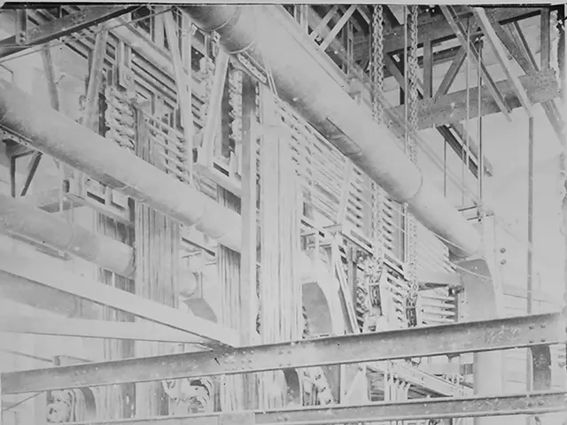 The image shows a black and white photo of a factory with pipes, rods, and other objects. At the...