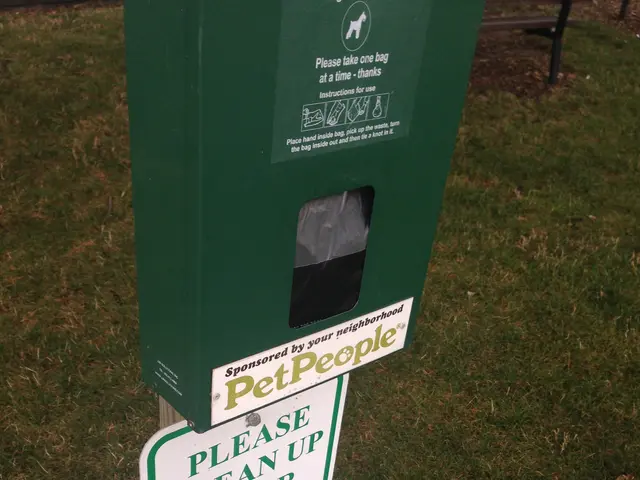 The image shows a green trash can sitting on top of a grass covered field, with two boards attached...