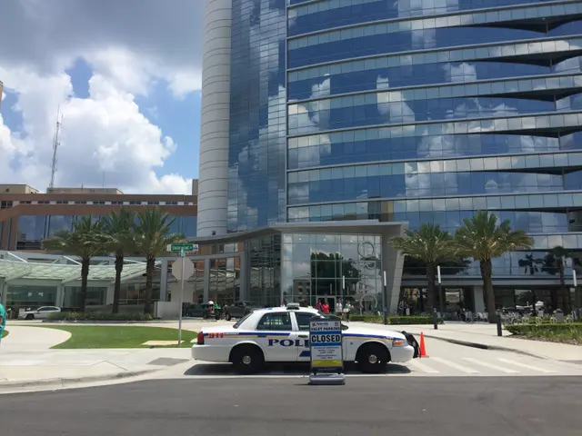 The image shows a police car parked in front of a large building with glass walls. There is a board...