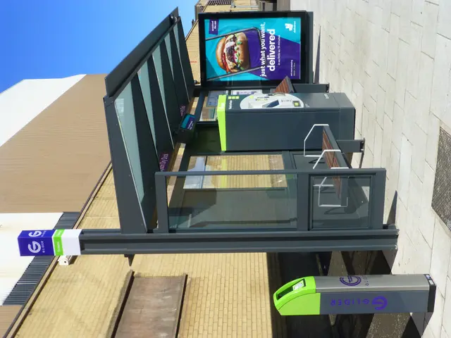 The image shows a bus stop with a large screen on the side of it, surrounded by buildings, trees,...