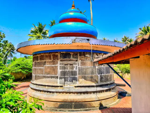 The image shows a small building with a blue dome on top of it, surrounded by lush green plants and...