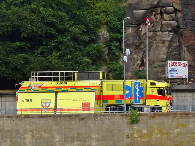 The image shows an ambulance parked on the side of a road next to a cliff, with a wall, railing,...