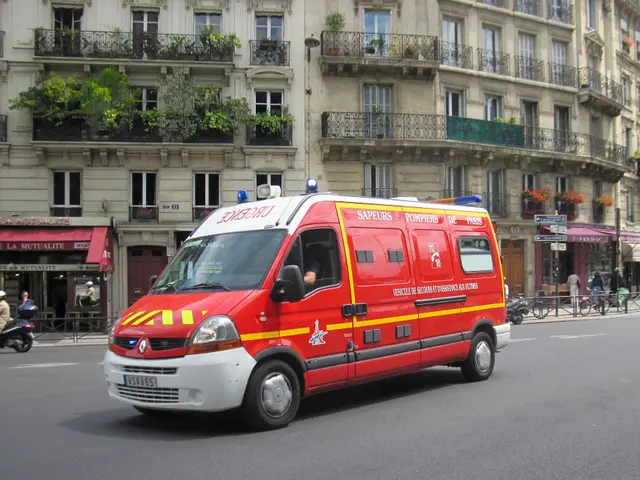 The image shows an ambulance parked on the side of the road in front of a building with windows,...