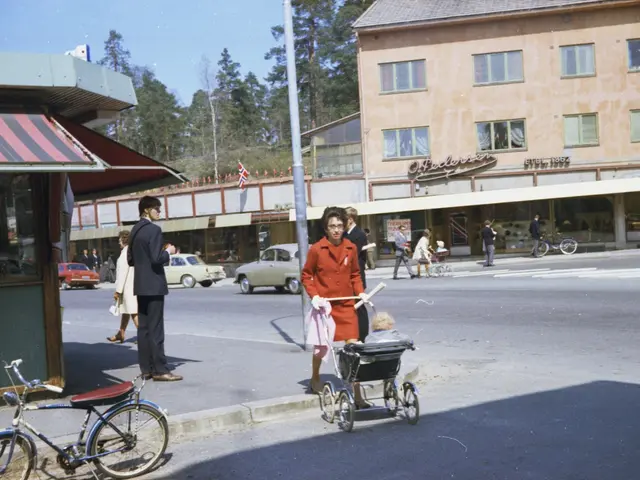 The image shows an old photo of a woman pushing a baby in a stroller down the street, surrounded by...