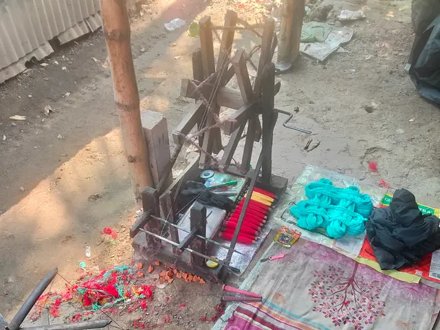 The image shows a wooden spinning wheel sitting on top of a dirt ground next to a pile of clothes,...