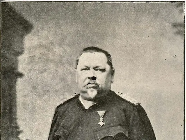 The image shows an old black and white photo of a man in uniform, standing and holding something in...