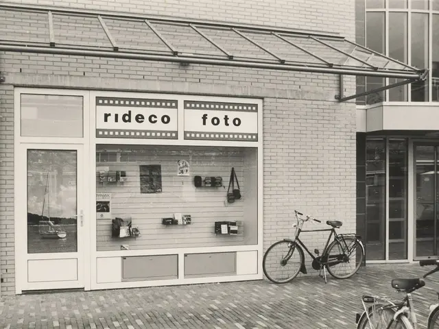 The image shows a black and white photo of two bicycles parked in front of a store. The store has...