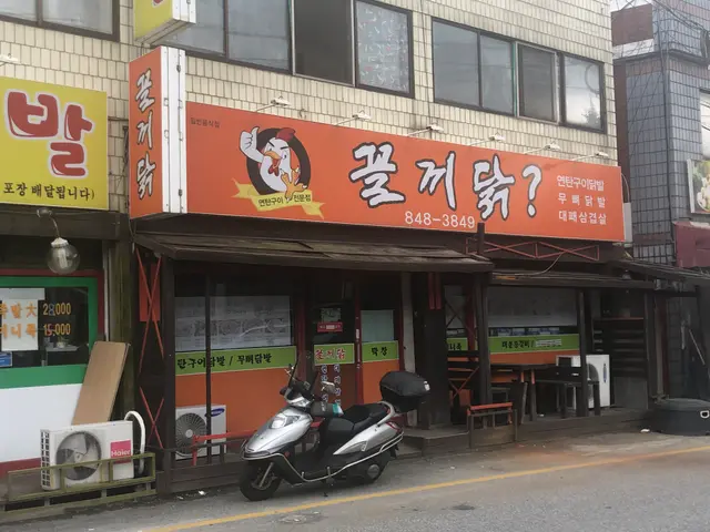 The image shows a scooter parked in front of a building with a sign on it. The building has windows...