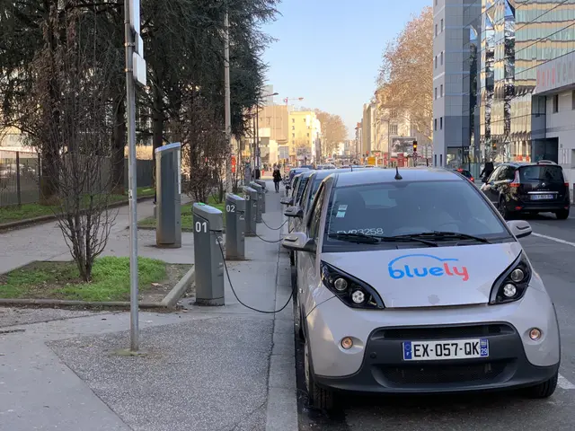 The image shows an electric car parked on the side of a street, surrounded by buildings, trees,...
