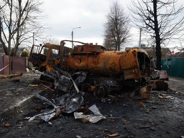 The image shows a burnt out truck sitting in the middle of a street, surrounded by scrap on the...