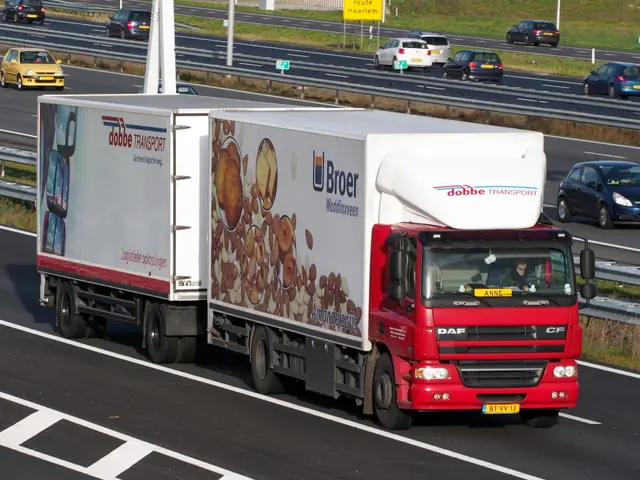The image shows a red and white truck driving down a highway next to other cars. There are poles,...