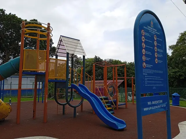 The image shows a playground with a blue slide and a yellow slide in the middle of it, surrounded...