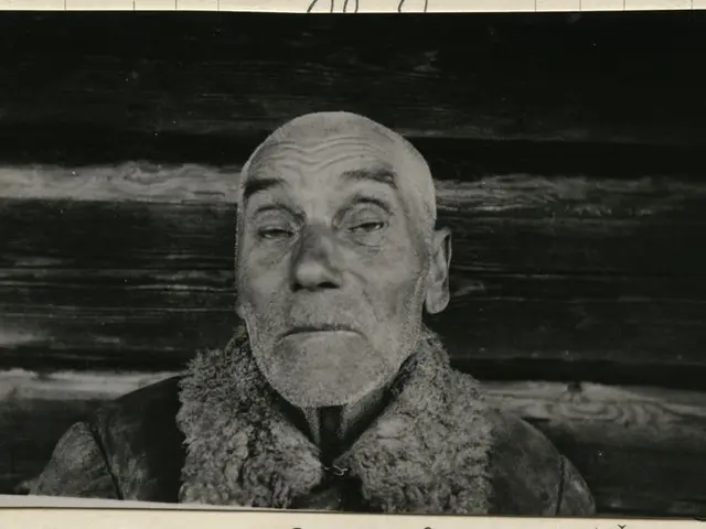 The image shows a black and white photo of a man with a beard wearing a jacket. At the bottom of...