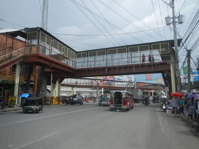 The image shows a busy street with a pedestrian bridge over it. There are vehicles on the road,...