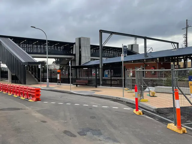 The image shows a train station with a bridge in the background, street poles, street lights,...