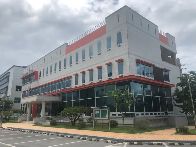 The image shows a large building with a lot of windows on the side of it, surrounded by street...