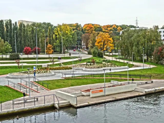 The image shows a river running through a lush green park next to tall buildings, with trees,...