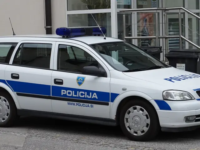 The image shows a white and blue police car parked in front of a building with glass doors and...