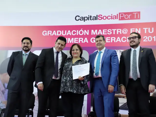 The image shows a group of people standing next to each other in front of a screen, with a woman in...