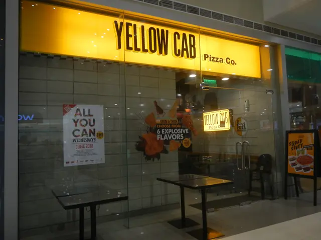 The image shows a yellow cab pizza co in the middle of a mall, with tables and chairs in front of...