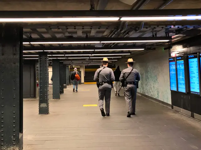 The image shows two police officers walking through a subway station, wearing hats and carrying...
