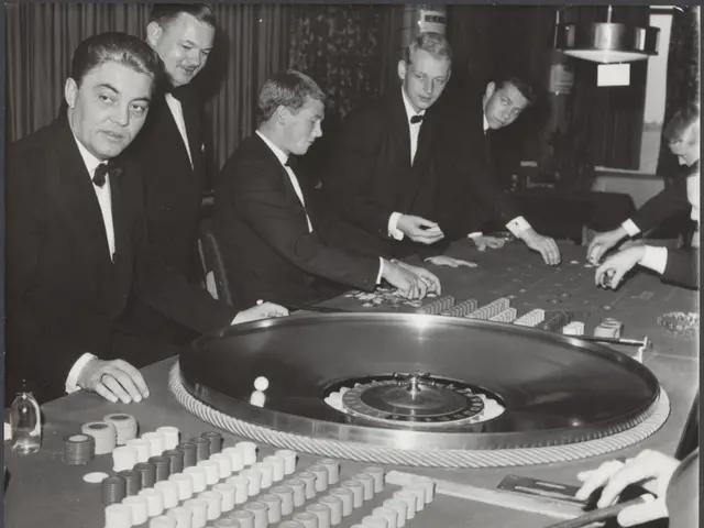 The image shows a group of men in tuxedos playing roulette at a casino. They are sitting around a...